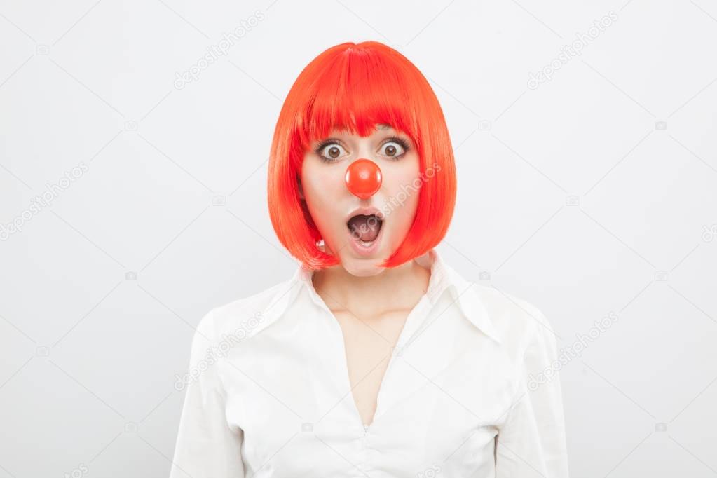 pretty young brunette caucasian woman with red nose and wig making a face surprised on white background