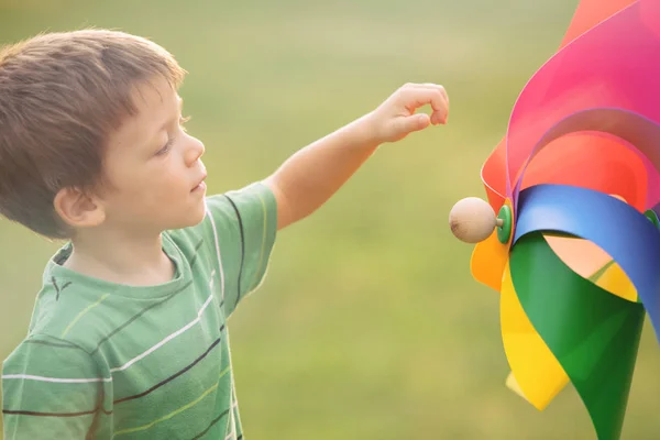 Bellissimo ragazzo biondo caucasico che gioca all'aperto al parco con girandola colorata — Foto Stock