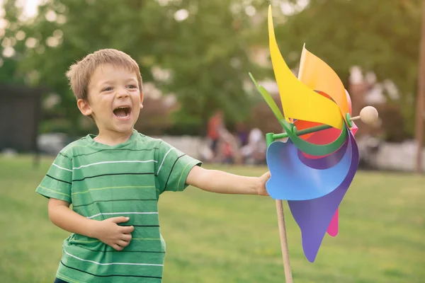 Beautiful caucasian blond kid playing outdoor at park with colorful pinwheel — Stock Photo, Image