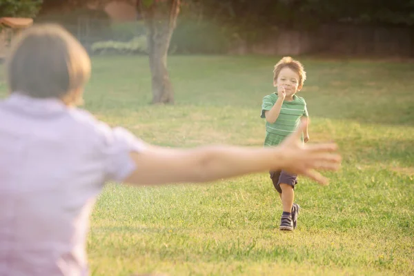 Feliz sonriente rubio caucásico niño al aire libre en parque corriendo y jugar con su mamá — Foto de Stock