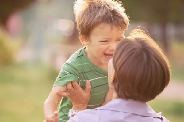 Glücklich lächelnde blonde kaukasische Kind draußen im Park laufen und spielen mit seiner Mutter — Stockfoto