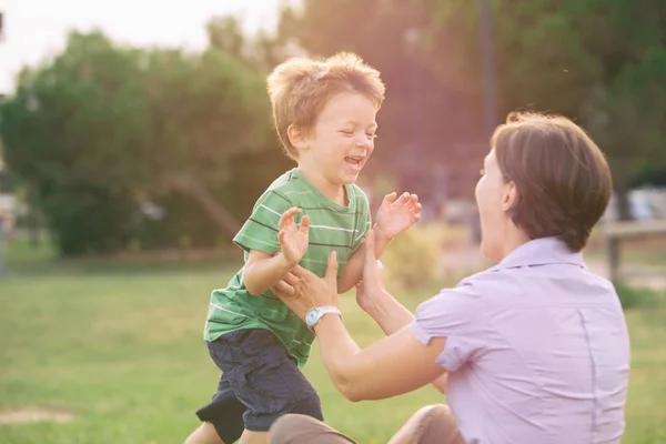 Счастливый улыбающийся белокурый белый ребенок на открытом воздухе в парке бегает и играть со своей мамой — стоковое фото