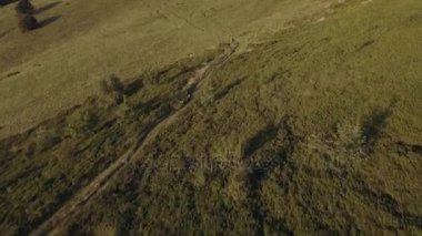 Motorcu iz sürmek offroad yolu üzerindeki ahşap orman valley yakınındaki dağ bisikleti tarafından yaz güneşli gün, yaklaşan günbatımı veya gündoğumu şafak veya robot alacakaranlık 4 k hava izleyin uçuş geniş vurdu