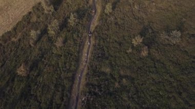 Motorcu iz binmek offroad yolda ahşap orman valley yakınındaki dağ bisikleti yukarıdan tarafından yaz güneşli bir günde, gündoğumu veya günbatımı şafak veya alacakaranlık 4 k yaklaşan hava dron genel gider uçuş geniş vurdu