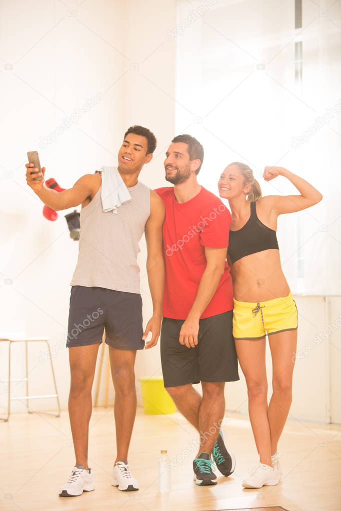 Group of young sporty people make a selfie with smartphone in gym