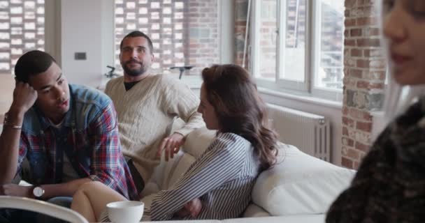Amigos multiétnicos pessoas conversando tomar café da manhã e relaxar no sofá interior na moderna casa industrial. 4k handheld câmera lenta de vídeo — Vídeo de Stock