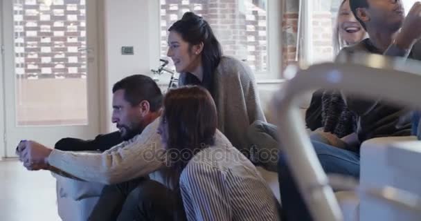 Багатоетнічна група друзів люблять розслаблятися на дивані, граючи у відеоігри та розважаючись у приміщенні в сучасному індустріальному будинку. 4k портативний відеозапис — стокове відео