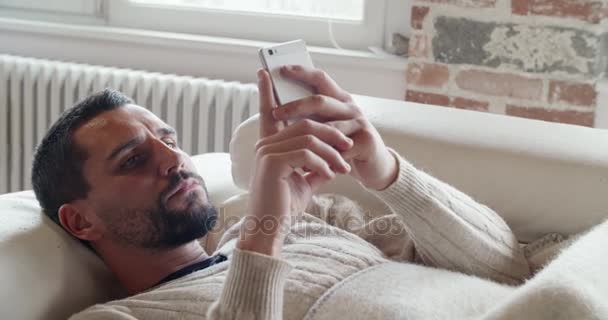 Young caucasian man detail relaxing on couch using smartphone indoor in modern industrial house. 4k handheld  close up video shot — Stock Video