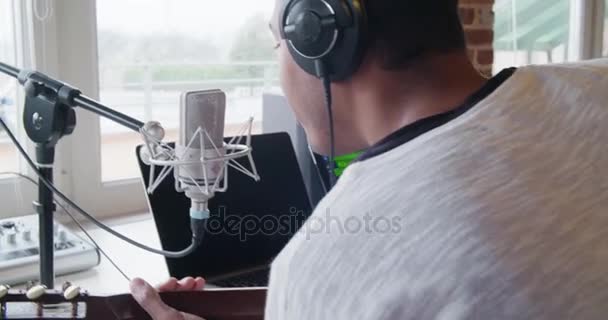 Black man creative musician at home studio works by playing, singing and recording guitar with notebook tablet and microphone indoor in modern industrial house. 4k handheld back vídeo tiro — Vídeo de Stock