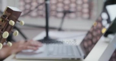 kadın yaratıcı müzisyen ev stüdyosunda oynayan, şarkı ve gitar ile defter tablet ve mikrofon kapalı modern evde kayıt çalışır. Beyaz esmer. 4 k el yan kapatın video