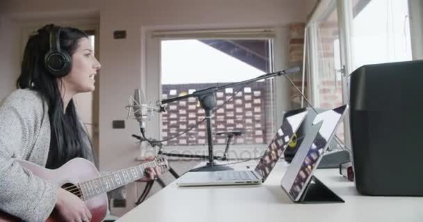 Женщина творческая музыкант в домашней студии работает, играя, пение и запись гитары с ноутбука планшета и микрофона в помещении современного промышленного дома. белая брюнетка. 4k портативное боковое видео — стоковое видео
