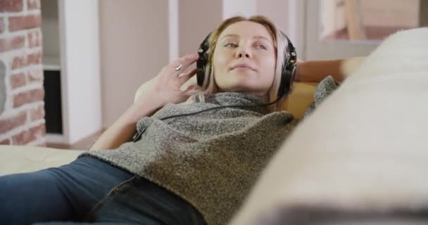 Mujer escuchando música con auriculares en el sofá — Vídeo de stock