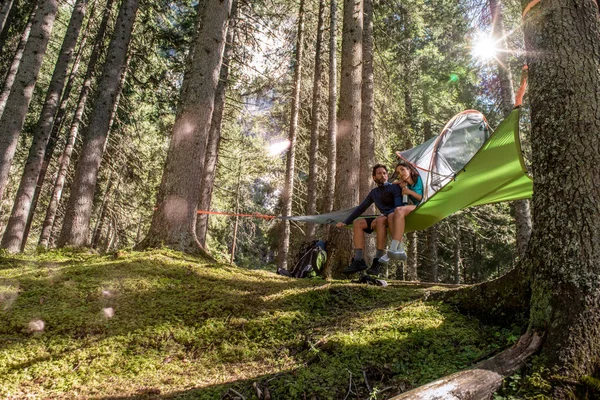 couple relaxing in hanging tent camping in forest