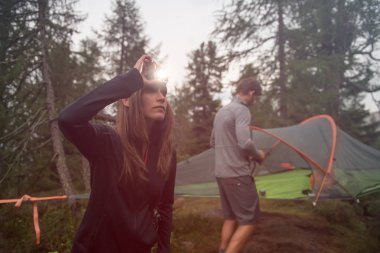 Woman turning on headlamp flashlight near hanging tent camping. Group of friends people summer adventure journey in mountain nature outdoors. Travel exploring Alps, Dolomites, Italy. clipart