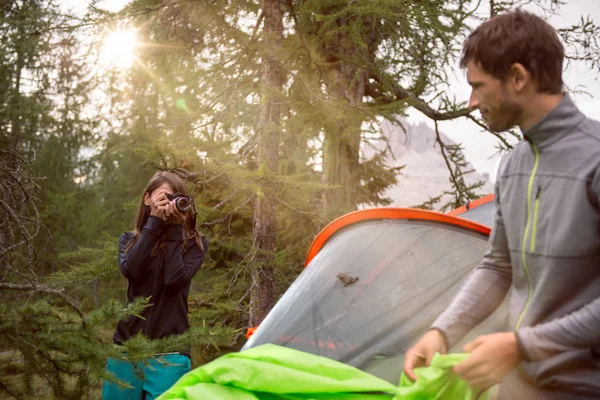 Kvinnan tar foto av mannen nära hängande tält camping med solen flare. Grupp av vänner personer sommar äventyr resa i berg naturen utomhus. Resa utforska Alperna, Dolomiterna, Italien. — Stockfoto