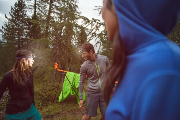 Man och kvinna skämtar och leende med strålkastare i kväll nära camping. Grupp av vänner personer sommar äventyr resa i berg naturen utomhus. Resa utforska Alperna, Dolomiterna, Italien. — Stockfoto