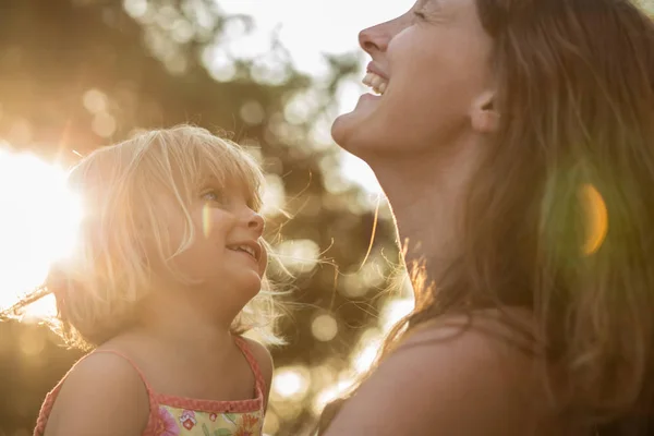 Молодая мама держит на руках блондинку-девочку и смеется или улыбается. Теплый закатный свет. Семейный летний отдых в море или океане — стоковое фото