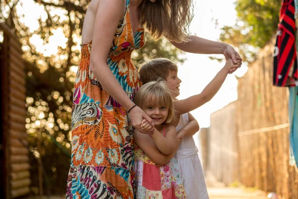 Ung mamma hålla hennes blonda dotter flickor på hennes armar leende. Varma solnedgången ljus. Familjens sommar resor semester på havet eller havet — Stockfoto