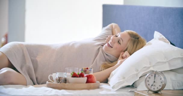 Bella donna che fa colazione con yogurt, frutta e cereali sul letto. Mattina svegliarsi a casa in camera da letto. Gente caucasica sdraiata sul letto. 4k video — Video Stock