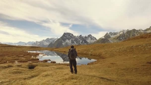 Uomo fotografo escursionista sparare foto vicino al lago per monti innevati.Dietro vista. Giornata autunnale soleggiata Escursioni nella colorata foresta rossa natura selvaggia montagna all'aperto.Alpi Parco lacustre Devero. 4k video — Video Stock