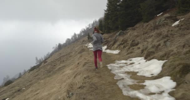 Αθλητής κορίτσι τρέχει μέσα από το χιονισμένο μονοπάτι. Μετά πίσω. Πραγματικοί άνθρωποι γυναίκα αθλητισμού δρομέας κατάρτιση το φθινόπωρο ή το χειμώνα στην άγρια ορεινή ύπαιθρο φύση, κακό ομίχλη weather.4k 60p βίντεο αργής κίνησης — Αρχείο Βίντεο