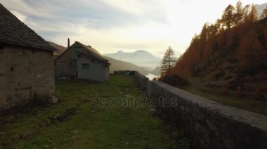 Yürürken Pov günbatımında güneş parlama ile yolu lodge, valley Gölü ve karlı bağlar düşmek. Güneşli sonbahar günü renkli kırmızı orman vahşi doğa dağ outdoors.4k'da yürüyüş gelin görünümü kurulması video