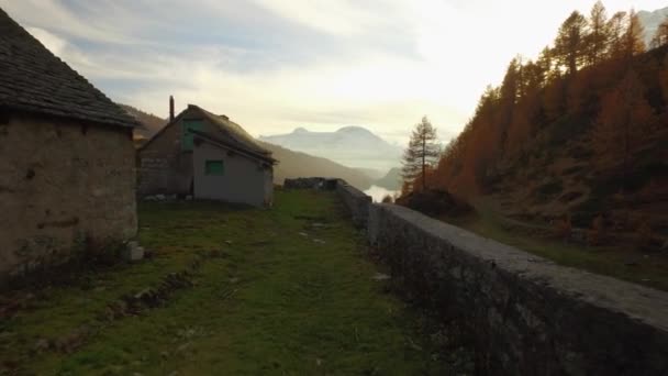 POV walking on fall path to lodge,valley lake and snowy mounts at sunset with sun flare.Sunny autumn day Hiking in colorful red forest wild nature mountain outdoors.4k point of view establishing video — Stock Video