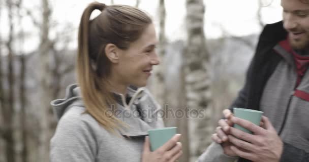 Mujer trayendo bebidas calientes o café o té al hombre en el lugar de acampada. Pareja de personas enamoradas de otoño viaje al aire libre en la naturaleza. Día soleado de otoño. 4k video en cámara lenta — Vídeo de stock