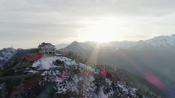 Körüli pályára épület vagy templom havas hegy tetején az ősszel vagy télen napnyugtakor. Fenyves erdőben és a szabadtéri havas hegyek légi establisher.4k drone repülés létrehozó lövés — Stock videók