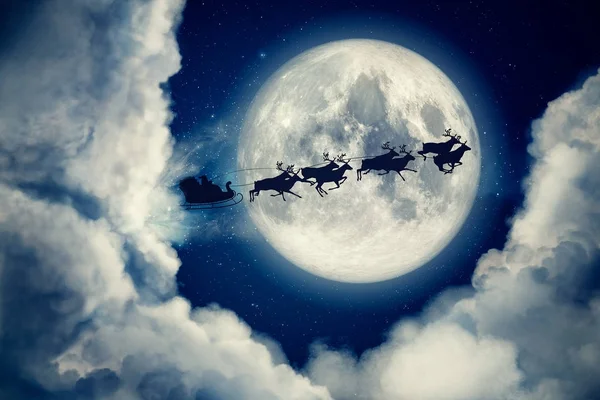 Blue Xmas Eve night with moon and clouds with Santa Claus sleight and reindeer silhouette flying to bring gifts and presents with text space to place logo or copy. Открытки с подарком на Рождество — стоковое фото