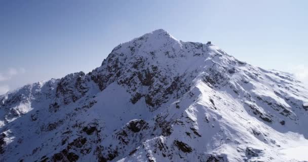 Flyg flyga flytta bakåt över snötäckta berg peak ridge herrgårdsarkitektur. Utomhus snö alpina vilda naturen scape i vinter. 4 k drone flygning upprättar skott — Stockvideo