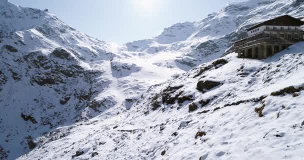 Vuelo aéreo moviéndose hacia atrás sobre el valle nevado de la cresta de la montaña cerca del establecimiento de la cabaña. Nieve al aire libre alpino paisaje de la naturaleza salvaje en invierno. vuelo drone 4k estableciendo disparo — Vídeo de stock