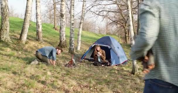 Man verlichting haard terwijl vriend hout logs.real vrienden brengen mensen buiten camping tent vakantie in herfst reis. Zonnige herfstdag in natuur, saamhorigheid en vriendschap. 4k video — Stockvideo