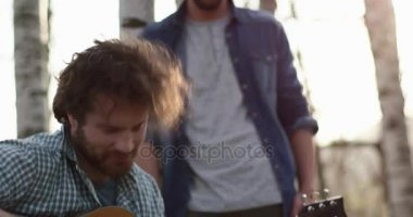 Adam gitar yangın place.real dost insanları birbirine yakın çevresinde açık hava kamp çadır tatil sonbahar gezisi oynayarak rahatlatıcı. Sonbahar güneşli bir günde doğa, beraberlik ve dostluk. 4k video