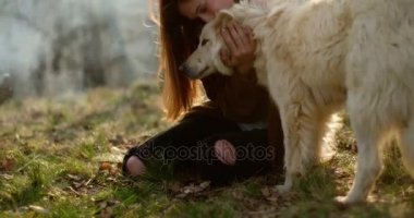 Yangın place.real arkadaşlar insanlar açık hava kamp çadır tatil sonbahar gezi çevresinde mutlu kadın yavaşça okşayarak beyaz köpek gülümsüyor. Sonbahar doğa, hayvan dostluk güneşli günü. 4k video