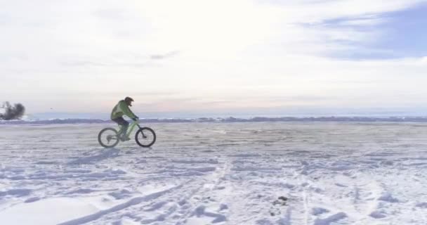 Side aerial over biker man cycling on snowy path during winter with mtb e-bike. Cyclist on bike on snow outdoors in winter. 4k drone flight video — Stock Video
