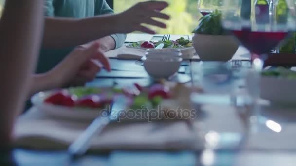 Detalhe sobre a louça.Quatro amigos caucasianos pessoas mediterranean salada italiana, bife de carne e pão almoço ou jantar. Festa de verão em casa na casa moderna 4k handheld vídeo — Vídeo de Stock