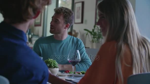 Personas bebiendo, comiendo y hablando.Cuatro amigos caucásicos hombre y mujer ensalada italiana mediterránea, filete de carne y pan almuerzo o cena. Fiesta de verano en casa en casa moderna 4k video portátil — Vídeo de stock