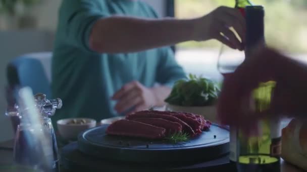 Homem dando garrafa de vinagre para amigo.Quatro amigos caucasianos pessoas salada italiana mediterrânea, bife e pão almoço ou jantar. Festa de verão em casa na casa moderna 4k handheld vídeo — Vídeo de Stock