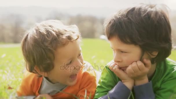 Šťastné děti s úsměvem zblízka portrét. Dvě děti bratra, smát a hrát zároveň ležel travní luční ve venkovní slunečný den. Rodinné syn chlapci v nature.video záběry — Stock video