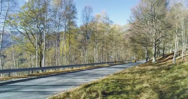 Backward aerial view over yellow vintage car travelling on road in colorful autumn forest.Fall orange, green, yellow red tree woods.Mountains street path establish isher.4k drone flight establishing shot — стоковое видео