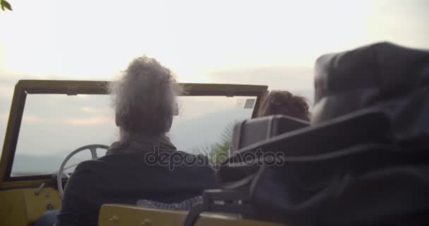 Homem e mulher levantando o braço em carro olhando pôr do sol. Visão traseira. Casal caucasiano no amor roadtrip férias italiano viagem no conversível carro do vintage — Vídeo de Stock