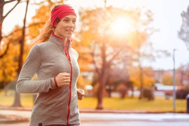 koşu egzersiz eğitim genç güzel beyaz bir kadın. Sonbahar çalışan fitness kız şehir kentsel park ortamında fall ile portakal ağaçları. Gündoğumu veya günbatımı sıcak ışık. Sezon soğuk spor aktivite