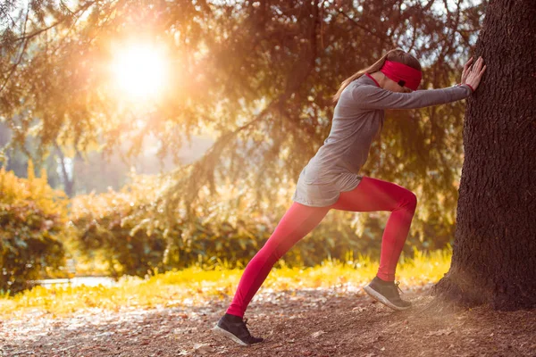 Jovem bela mulher caucasiana alongamento treino. Autumn running fitness girl in city urban park environment with fall trees orange. Pôr do sol ou nascer do sol luz quente. Conceito de actividade desportiva — Fotografia de Stock