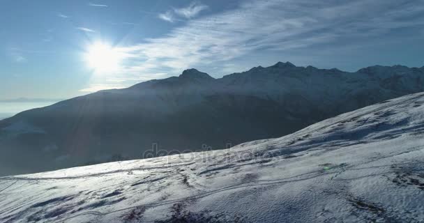 Vorwärts Luftaufnahme von oben über schneebedeckten Winterberg mit Skipisten bei sonnigem Tag mit Wolken. Hintergrundbeleuchtung weiße Alpen Berge Schnee Saison Errichter mit Sonnenschein.4k Drohnenflug Einrichtungsaufnahme — Stockvideo