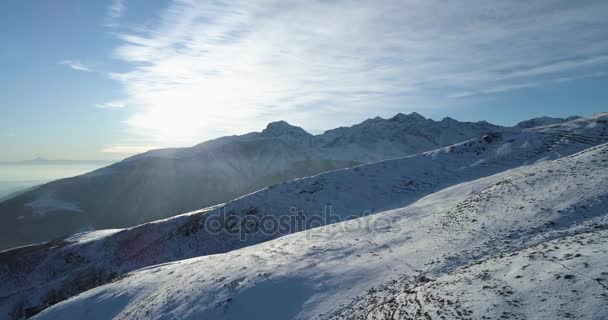 Vista superior aérea hacia adelante sobre la montaña nevada de invierno con pistas de esquí en el día soleado con nublas.Luz de fondo blanco Alpes montañas nieve temporada Establecimiento con sol brillante.4k drone vuelo establecer tiro — Vídeos de Stock