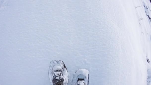 Над головой POV человек пеший туризм и ходьба в снегоступах на открытом воздухе по белой снежной тропинке в горах дикого поля зимой. Ноги и обувь шагают по снегу. — стоковое видео