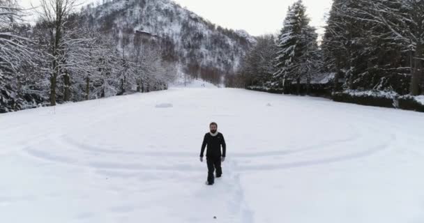 在冬天, 在松树林森林附近, 雪在积雪覆盖的田野上行走的人向后空中。欧洲阿尔卑斯山户外自然景观雪山. 徒步旅行者 4 k 无人机飞行 — 图库视频影像