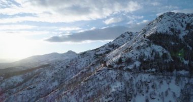 Yan yörünge hava üstten görünüm kışın beyaz kar dağda. Orman orman. Karlı dağlar sokak yol ILDIZ. Gündoğumu veya günbatımı güneş backlit.4k robot uçuş düz aşağı kurulması atış