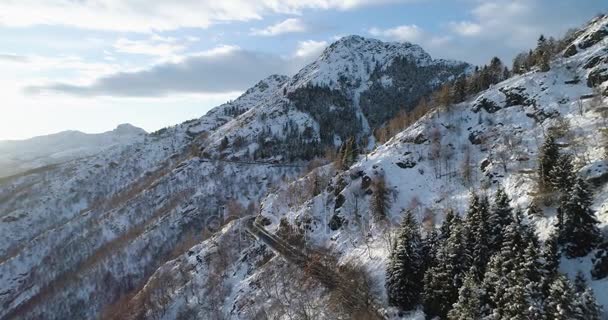 在森林森林附近的冬季雪山上, 前方的汽车行驶在公路上的俯视图。雪山路制订。日落或日出太阳背光. 4 k 无人机飞行建立射击 — 图库视频影像